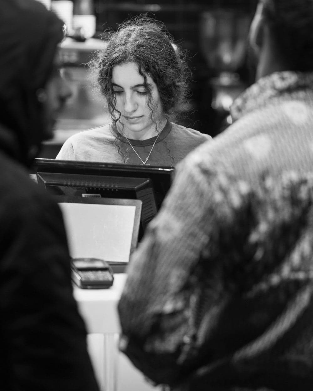 Atendente no caixa de uma loja, com clientes à frente.
